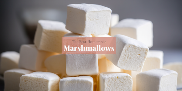 Soft and fluffy homemade marshmallows cut into squares, dusted with powdered sugar, and stacked on a wooden cutting board.